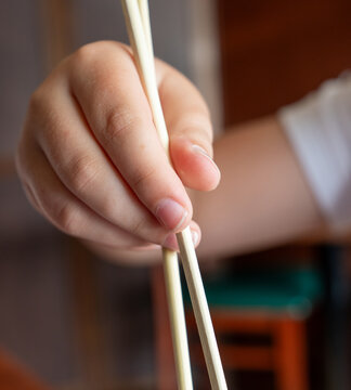 Close Up of Hand Holding Wooden Chopsticks in Sushi Restaurant