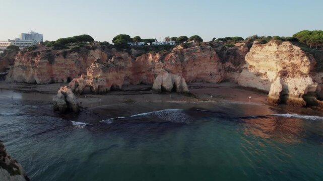 Stunning aerial view flying over the scenic cliffs and rock formations of Praia dos Tres Irmaos beach in Alvor, Algarve region of Portugal