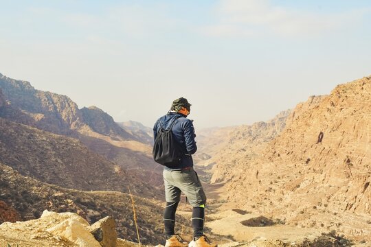 Man trekker standing on cliff edge using mobile phone network coverage vast sandstone valley mountain landscape backdrop hiking travel tech concept Dana Reserve Jordan