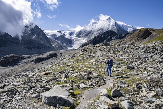 Hiker on rocky path with impressive views of snow-covered mountain landscape, Mont Blanc de Cheilon mountain summit with glacier in the back, H&eacute;rm&eacute;nence, Valais Alps, Switzerland