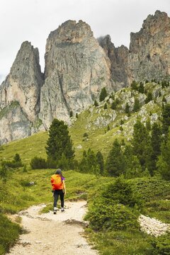 Female hiker with backpack walking dirt trail green alpine meadow majestic mountain peaks background Malga Rossalm Dolomites Italy summer adventure travel lifestyle