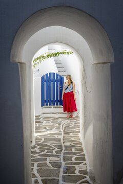 White archways between houses, Young woman with red dress in the old town of Lefkes, Paros, Cyclades, Greece