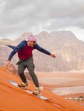 Man successfully sandboarding down steep red dune in Wadi rum showing skill balance confidence achievement and adventure Jordan