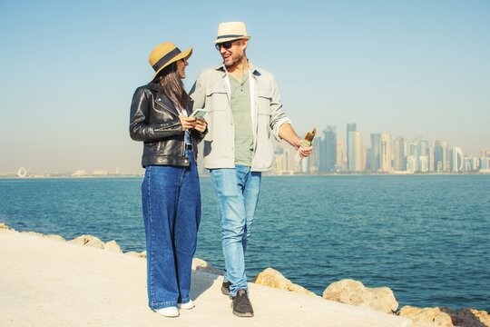 Doha Qatar tourist couple walking Corniche waterfront West Bay with skyline skyscrapers background happy tourists vacation lifestyle Middle East urban city exploration sunny summer fun day bonding