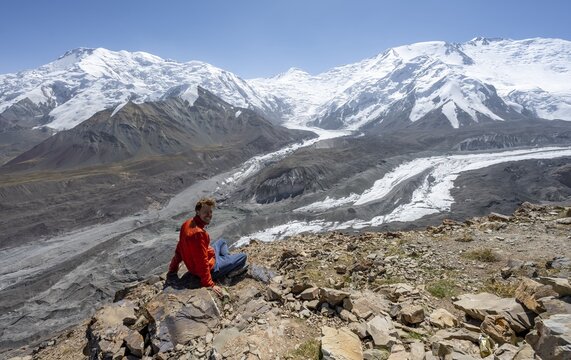 Mountaineer at Traveller's Pass with view of impressive mountain landscape, high mountain landscape with glacier moraines and glacier tongues, glaciated and snow-covered mountain peaks, Lenin Peak and Peak of the XIX Party Congress of the CPSU, Trans Alay Mountains, Pamir Mountains, Osh Province, Kyrgyzstan