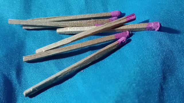 A vintage box of wooden matches with purple match heads, partially open with several loose matches scattered on a blue fabric surface, creating a simple nostalgic still life.
