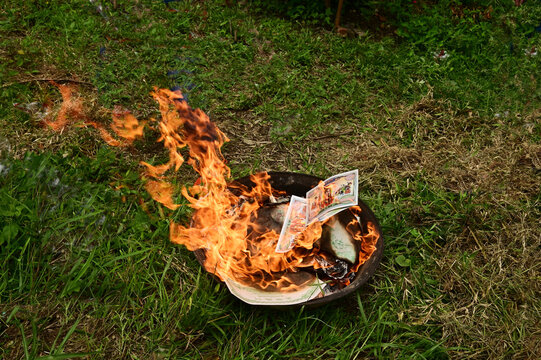 Ritual of burning joss paper, also known as ghost money, inside a metal container placed on the grass.
