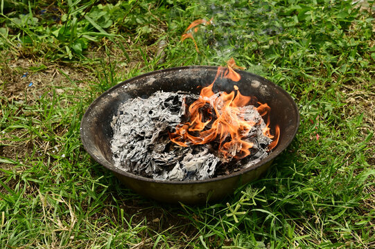 Ritual of burning joss paper, also known as ghost money, inside a metal container placed on the grass.