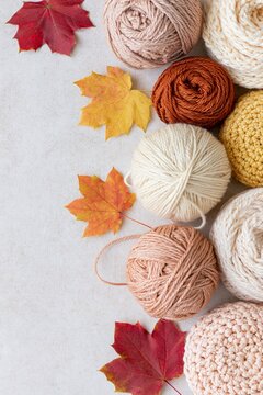 Cozy autumn flat lay with warm neutral yarn balls, knitted textures and colorful maple leaves arranged with copy space