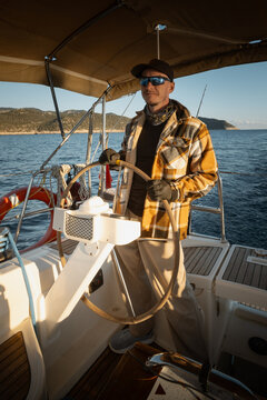 Young male captain standing at the helm of a sailing yacht and looking into the distance