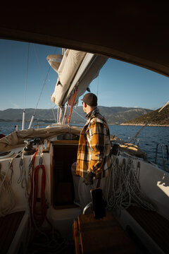 Young male captain standing at the helm of a sailing yacht and looking into the distance