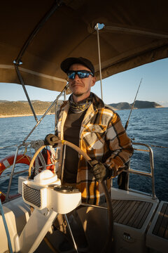 Young male captain standing at the helm of a sailing yacht and looking into the distance
