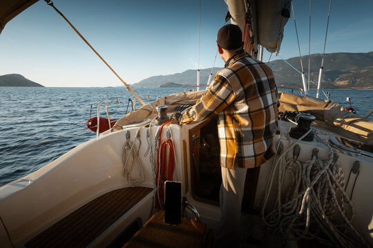 Young male captain standing at the helm of a sailing yacht and looking into the distance