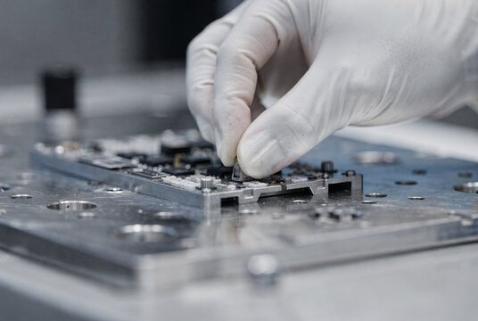 Technician's gloved hand assembling electronic components on a PCB.