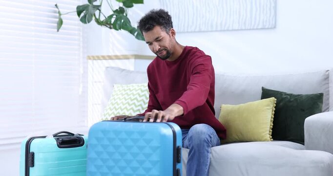 Man choosing between stylish suitcases on sofa indoors