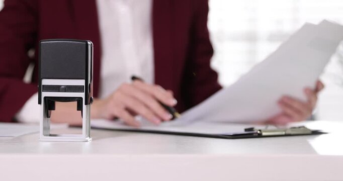 Notary checking and stamping documents at white table in office, closeup