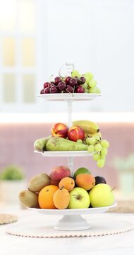 Fruit stand filled with mix of fresh juicy fruits on white marble table in kitchen, camera moving