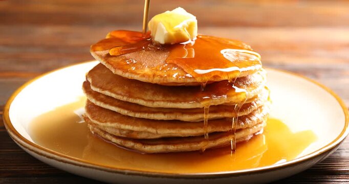 Pouring maple syrup onto pancakes with butter at wooden table, closeup