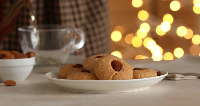 Woman pouring tea into cup and taking almond cookie from table, closeup