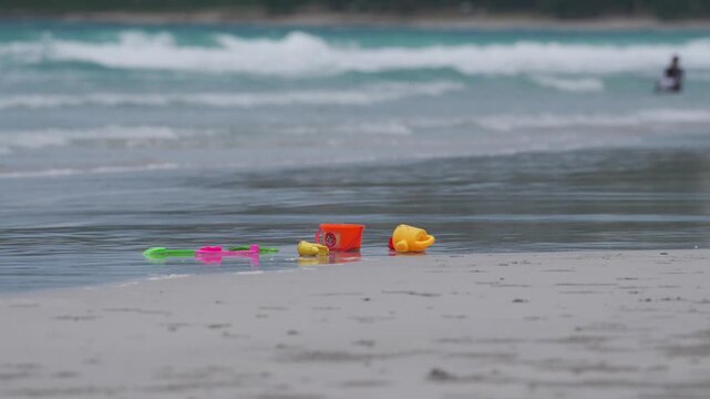 Beach ocean sand toy bucket shovel wave shoreline colorful plastic playset on wet shore after tide, gentle surf, quiet summer seascape, childhood nostalgia, family day memory