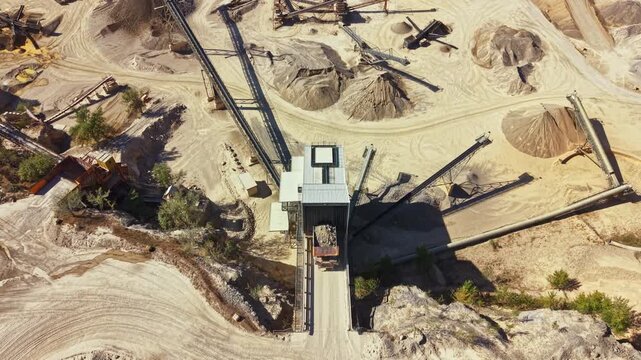 A sand and gravel site with piles of materials and industrial machinery at work. Conveyor belts transport materials among the various areas.