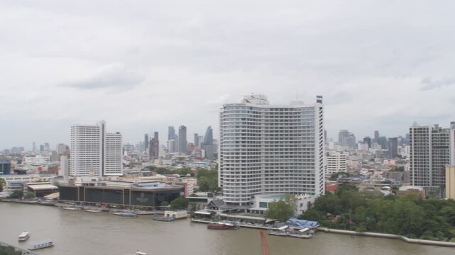 panoramic daytime cityscape view of modern skyscrapers, luxury hotels, and boats along the chao phraya river in bangkok thailan