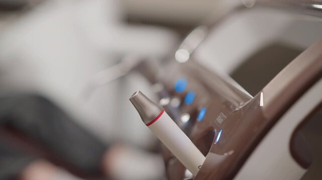 Close up of dental handpiece resting on sterilization tray in modern orthodontic clinic. Dental instrument with metallic tip and white body featuring red accent set against blurred