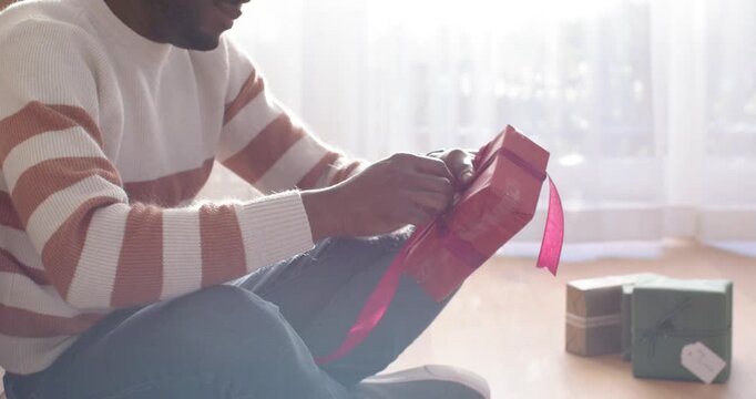 African American male sitting at window, finding loose knot and using tape dispenser, prepping gift