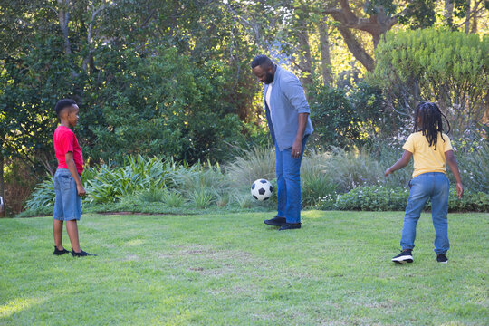 African American dad and two sons playing soccer in yard with black white ball wearing Tshirts