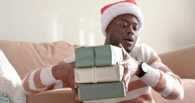 African American man in Santa hat catching falling gold parcel and steadying wrapped gifts on couch