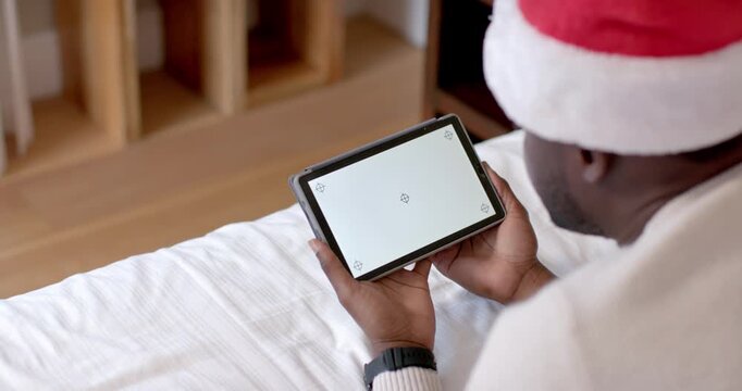 Man wearing Santa hat is adjusting grip and tilting tablet on bed to maintain screen focus