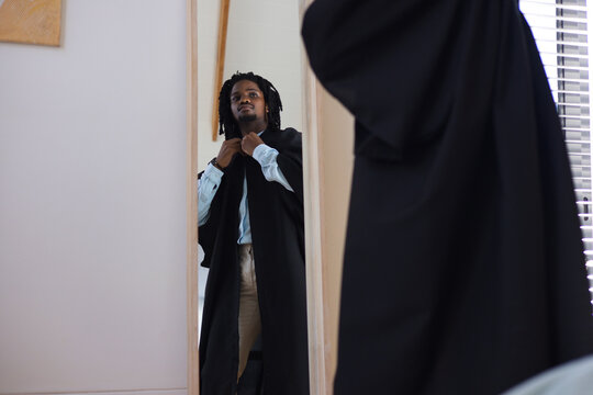 African American man standing adjusting black robe over light blue shirt in front of mirror