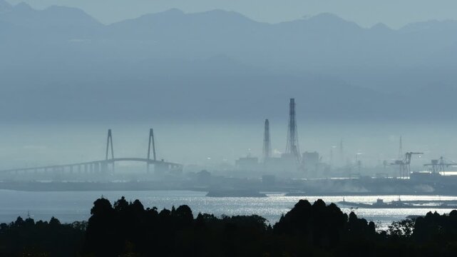 濃い霞（朝霧・黄砂）に包まれた新湊大橋と手前の森のシルエット