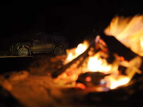 Off-road vehicle parked near glowing campfire at night copy space