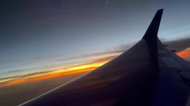 Commercial airplane flying through the beautiful sunrise sky, passenger point of view looking out the window at the winglet and the colorful horizon over the clouds