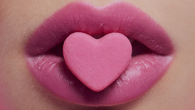 pink matte heart shape gummie inside beautiful woman lips	
