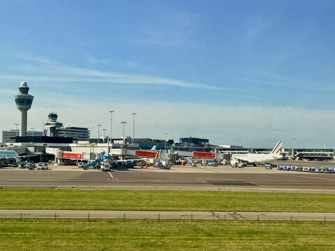 Schiphol, Netherlands, April 28 2025: Multiple aircraft are parked at the terminal of an airport under a clear blue sky on a sunny day. Activity and movement are visible