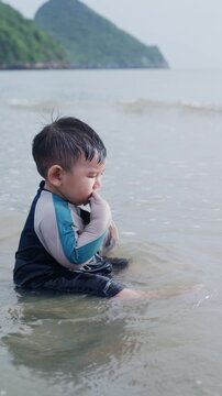 Cute baby boy wearing swimwear sitting in gentle sea waves vertical stock video.