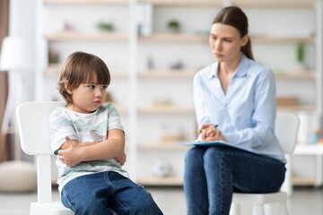 Worried Young Boy With Arms Crossed, Sitting In Therapy Session With Female Therapist In Healthcare...