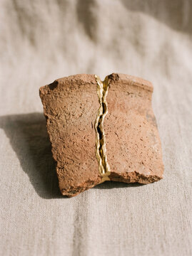 Kintsugi pottery shard repaired with gold lacquer on a textured linen background.