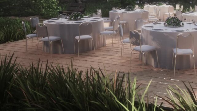 People set up tables with white cloths in a green area. Chairs are arranged around the tables. Some plants are visible in the foreground. A bench is nearby in the distance.