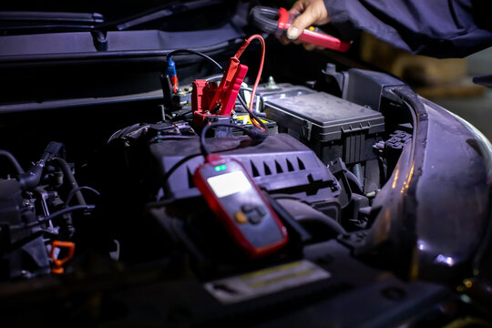 Selective focus to Jumper cable with Professional mechanic performing an on-site diagnostic test on a car battery using a digital tester and clamp meter to check health, voltage, and performance under