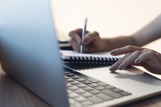 Close up of woman writing in notebook while using laptop, remote work and productivity concept.