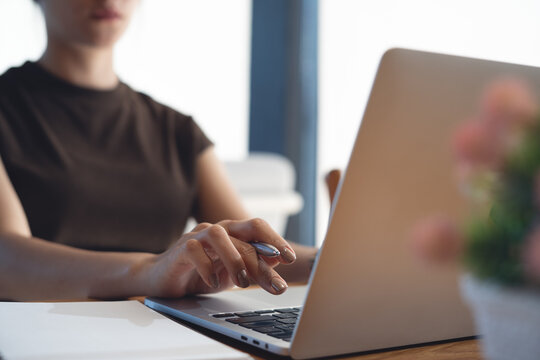 Woman working on laptop with notebook on wooden desk in modern workspace, remote work, online business concept. close up