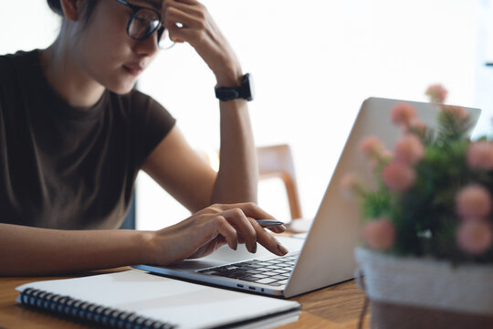 Stressed woman working on laptop at desk, holding pen and touching forehead, remote work pressure and concentration concept.
