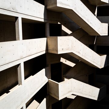 Abstract brutalist concrete building facade featuring geometric zig-zag stairs and strong architectural sunlight shadows.   