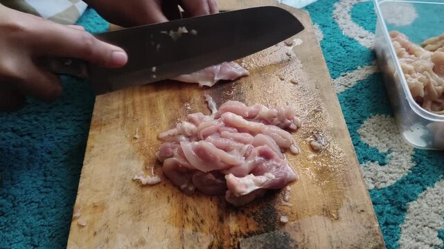 Close-up shot of kitchen food prep showing a knife cutting raw chicken or beef