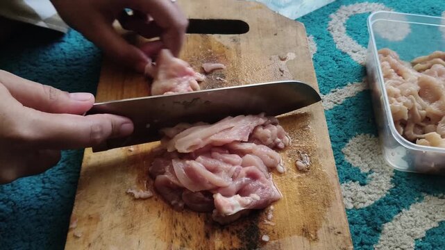 Close perspective of hands dicing fresh raw poultry on a wooden chopping block