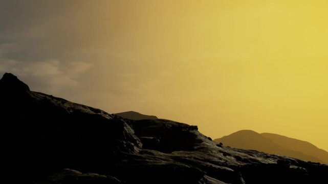A view shows rocks in the foreground with hills in the background. The sky changes colors as the sun sets above the landscape, creating silhouettes of the rocks and hills.