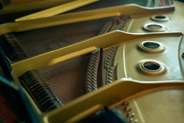 Close-up view inside a grand piano featuring a golden cast-iron plate alongside tensioned steel strings and metal tuning pins. © AncientAftertone